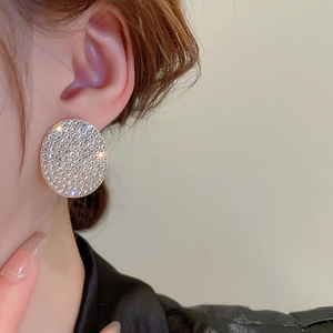 Close-up of a woman wearing luxury round gold stud earrings with pavé set white crystals