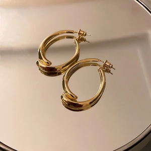 Macro shot of polished gold twisted oval earrings reflecting on a mirror surface