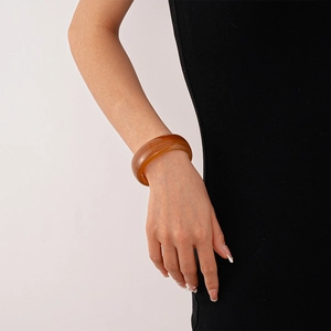 Detail view of a translucent amber acrylic cuff bracelet worn with a black dress