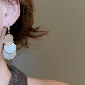 Detail of layered geometric round resin earrings worn by a model in warm light
