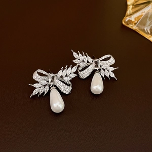 Close-up of bow earrings with sparkling cubic zirconia and drop pearls on leather