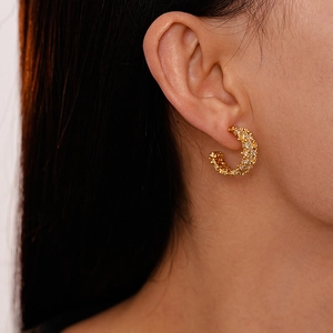Close-up of golden C-shaped textured earrings with sparkling zircon stones on model
