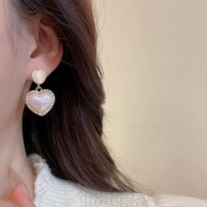 Close-up of heart-shaped opal and crystal earrings worn by a model in warm light