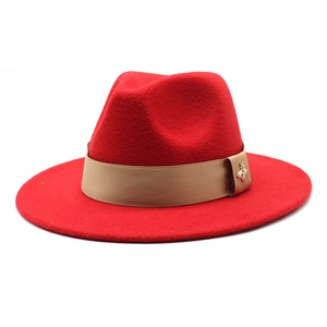 Macro view of a red wool fedora hat featuring a beige ribbon and a gold bee metal pin