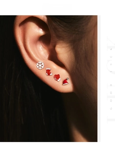 Detail view of four Christmas themed stud earrings worn on ear, including snowflake and hat