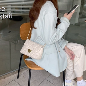 Detail of cream quilted crossbody bag with gold chain strap worn by a model in a cafe
