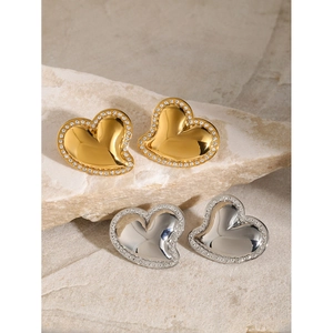 18k gold and silver heart-shaped earrings with rhinestones on light stone surface