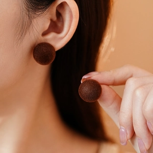 Close-up of elegant brown flocked round stud earrings worn by a model in soft lighting
