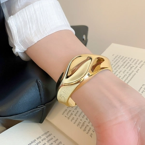 Macro detail of wide gold-plated acrylic cuff featuring irregular wave sculpture texture