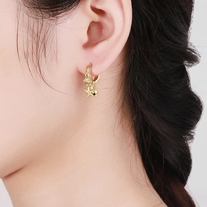 Detail shot of golden shell and starfish charms on hoop earrings worn by a model