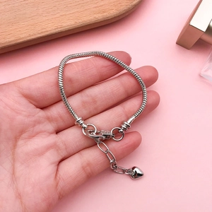 Detailed shot of silver snake chain bracelet with heart charm on hand over pink backdrop