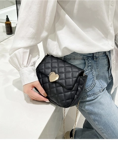 Detail of the heart-shaped gold buckle and quilted texture on the black chain bag