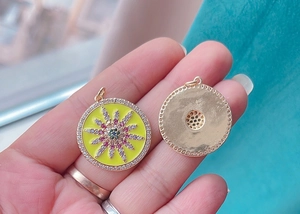 Macro shot of yellow enamel charms with colorful zircons and golden mesh texture back