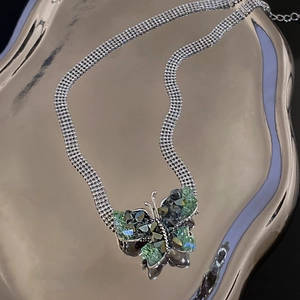 Macro view of butterfly pendant with green crystals on a silver-toned snake chain necklace