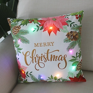 Christmas LED pillow with Merry Christmas text and festive floral wreath on a beige sofa