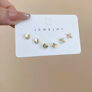 Detailed view of gold heart, cube and X-shaped stud earring set on jewelry display card