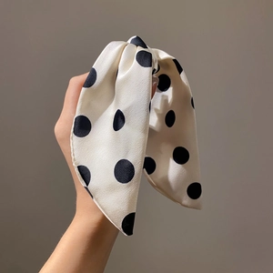 Close-up of cream polka dot silk bow hair claw clip held by hand against a grey wall