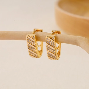 Detail of gold-plated V-shape earrings with pave-set zircons on a wooden branch