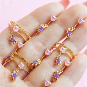 Close-up of golden rings featuring iridescent heart and purple teddy bear charms on hand