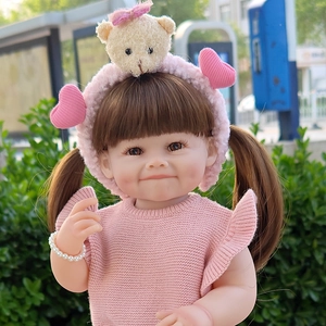 Close-up of 55cm reborn baby doll with brown pigtails in pink knit set and bear headband