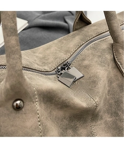 Close-up of dual square metal zippers on a taupe suede travel bag for women
