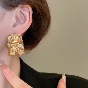 Close-up of a gold square earring with liquid metal texture and irregular fold design