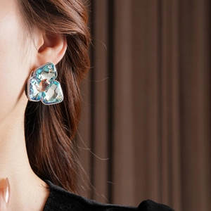 Detail of floral earring with blue crystals and orange gem worn on model ear