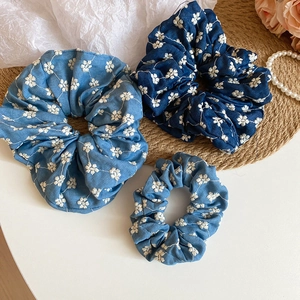 Detail of floral embroidery on denim fabric scrunchies in blue and light blue colors