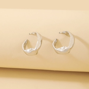 Detailed close-up of silver geometric C-hoop earrings featuring a molten lava texture
