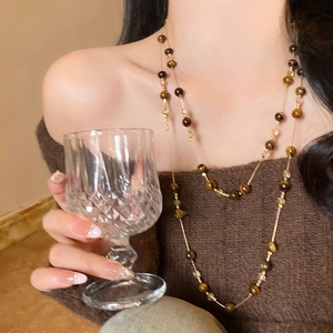 Detail of layered tiger eye beaded necklace on elegant model wearing knit sweater