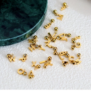 Flat lay of gold alphabet letter charms with bead loops on a white textured background