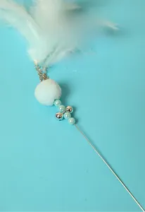 Detail of cat wand featuring white feathers, blue plush ball, bells, and beads