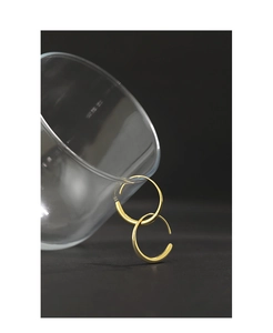 Minimalist golden hoop earrings resting on a glass edge against a dark artistic background