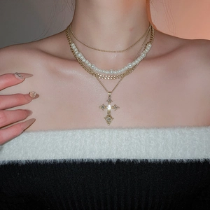 Close-up of layered necklace with cross pendant and pearls on a model wearing a sweater