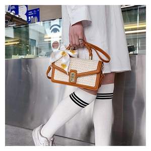 Detail of straw woven handbag featuring brown leather trim and golden metal clasp closure
