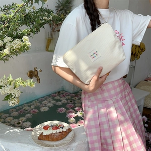 Detail of off-white corduroy makeup bag with embroidered label and gold zipper