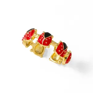 Gros plan sur une bague dorée ornée de coccinelles en émail rouge et noir brillant