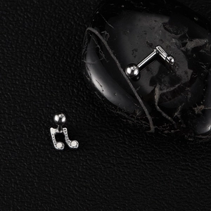 Close-up of silver musical note and straight bar stud earrings on a dark textured stone
