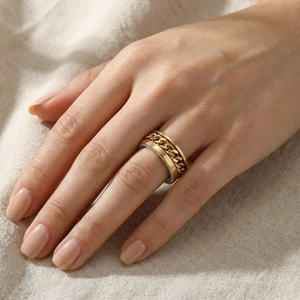 Détail d'une bague à maillons dorée sur un doigt avec un fond beige texturé élégant