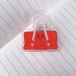 Detail eines roten Acryl-Binder-Clips mit lustigem Ausdruck auf Notizbuchpapier