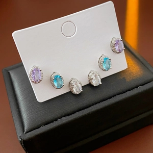 Close-up of oval zircon earrings in purple, blue, and clear colors on a display card