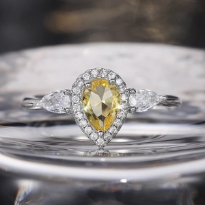 Macro shot of pear-shaped yellow zircon ring with halo diamonds on a reflective glass surface