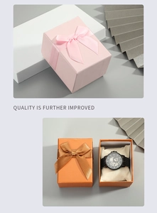 Detail view of pink and orange gift boxes with ribbon bows and a watch on a cushion