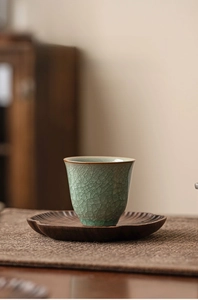 Detailed view of celadon bell-shaped tea cup with ice-crack glaze on wooden coaster