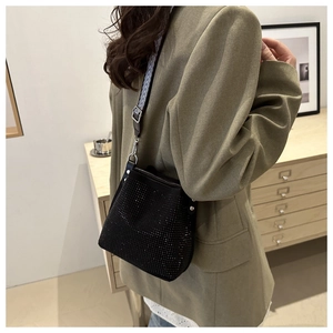Detail of black rhinestone bucket bag with geometric patterned wide strap on model