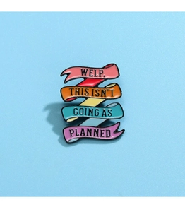 Detail of a rainbow enamel ribbon pin with text WELP, THIS ISN'T GOING AS PLANNED