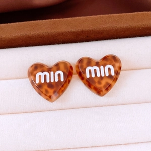Macro shot of heart-shaped acetate stud earrings with tortoiseshell pattern and miu logo