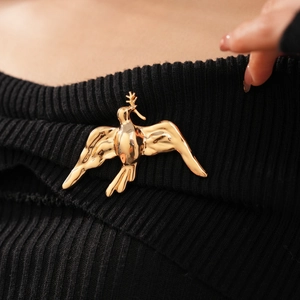 Detailed macro shot of a polished gold bird brooch pinned to a black knit sweater