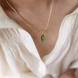 Close-up of gold snake chain with a green teardrop-shaped cat eye stone pendant worn by model