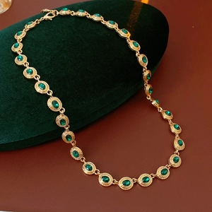 Détail d'un collier vintage doré avec pierres vertes ovales sur coussin en velours